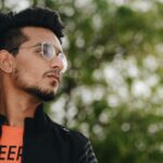 Portrait of a fashionable young man wearing glasses and a jacket outdoors with a natural bokeh background.